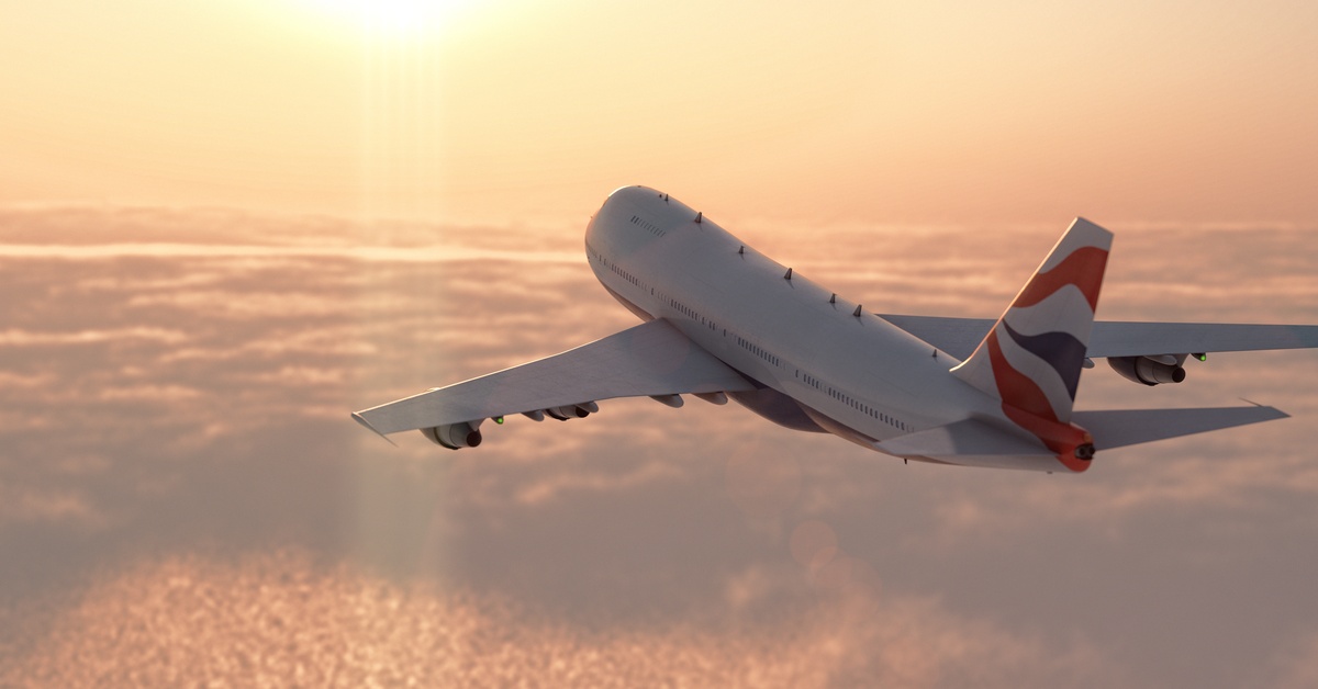 A white commercial aircraft moves through the yellow sky with wings extended and clouds beneath the plane.