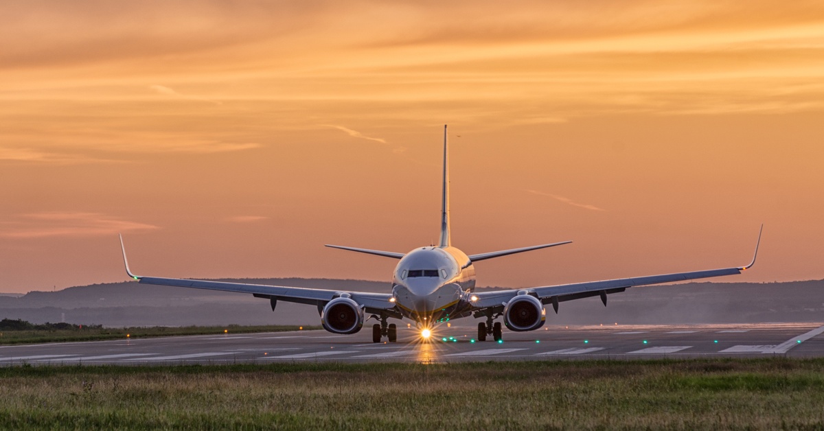 An airplane sitting on the runway for landing at sunset with orange light reflecting on the airport surface.