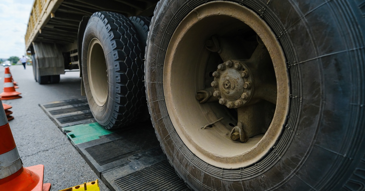 A close-up of large truck wheels positioned on a metal weighing scale platform with cones and road markings nearby.